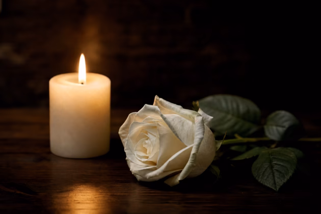 Brennende Kerze und weiße Rose als Zeichen der Trauer. Symbolbild. Foto: KI-generiert