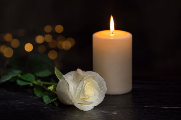 Brennende Kerze und weiße Rose als Symbol der Trauer um eine verstorbene Legende